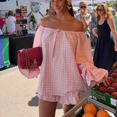 Woman in a pink checkered dress holding a red handbag at an outdoor market.